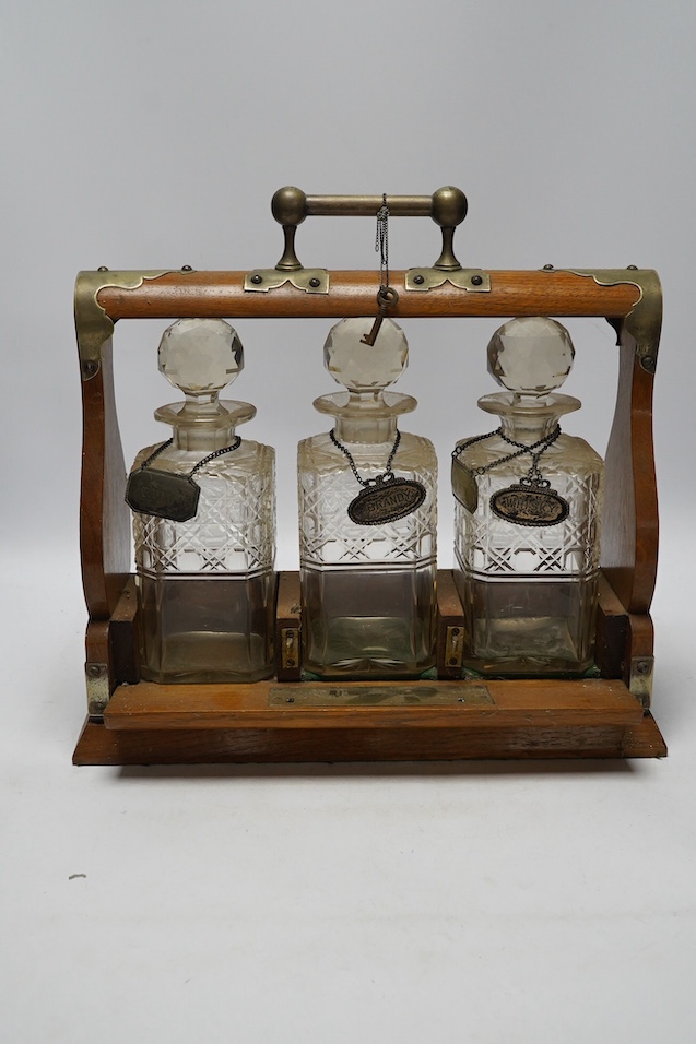 A Victorian oak three decanter tantalus with four spirit labels, and key, 37cm wide. Condition -fair